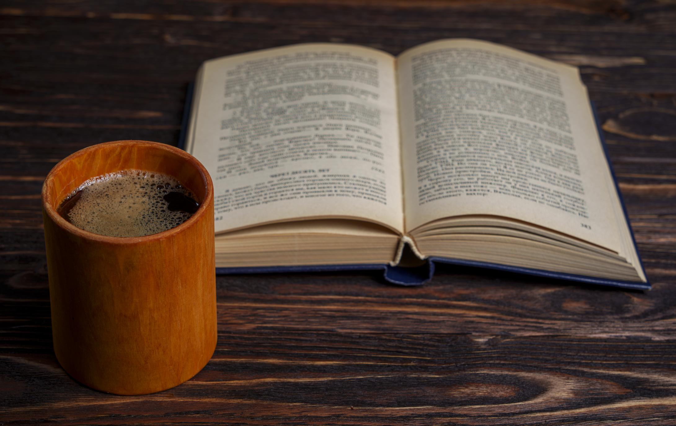 Open book and warm coffee on a wooden table.